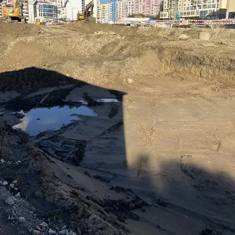 Excavation floor with standing water and a long shadow.