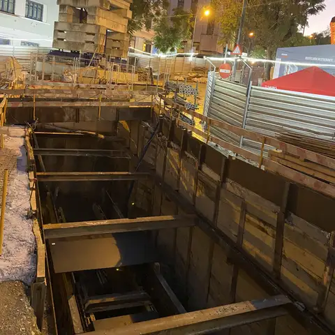 Deep excavation with steel shoring, lit at night.