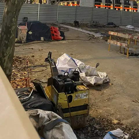 City construction site at dusk with a plate compactor and safety barriers.