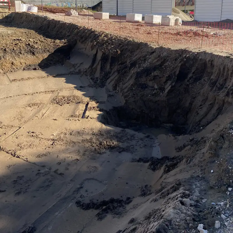 Open excavation with a sloped earth wall and a sandy floor.
