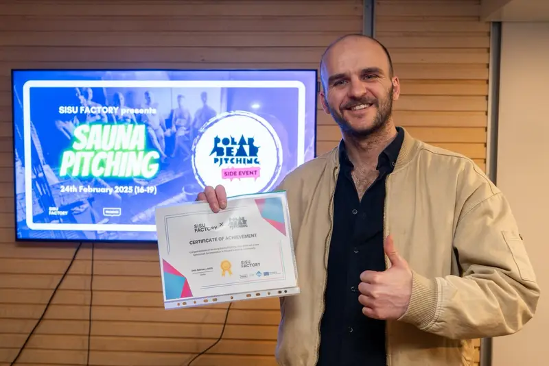 Endrit Kola holding the Sisu Factory certificate of achievement in front of the Sauna Pitching screen.